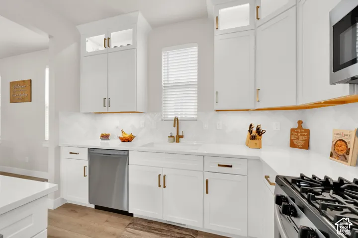 Kitchen featuring white Shaker-style cabinetry with glass-front uppers, solid-surface countertops, herringbone-patterned tile backsplash, wood-finish flooring, and metallic hardware