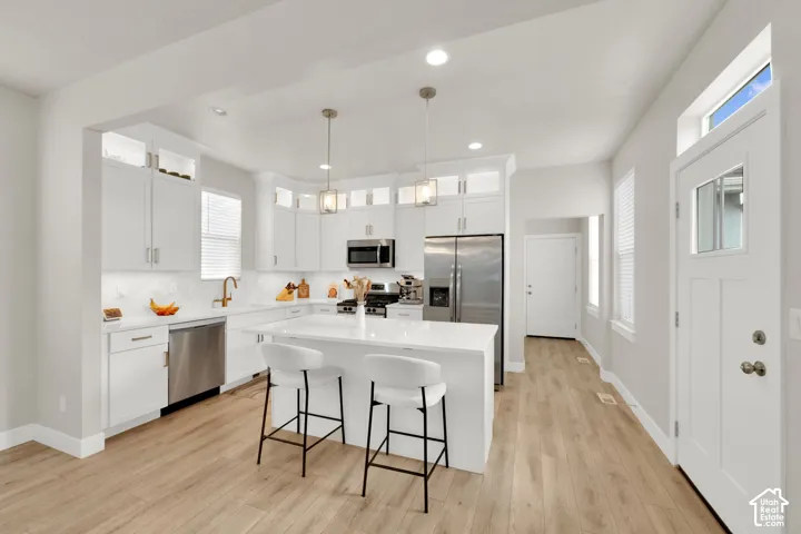 Kitchen featuring white shaker-style cabinetry, quartz countertops, stainless steel appliances, a central island, and wood-finish flooring