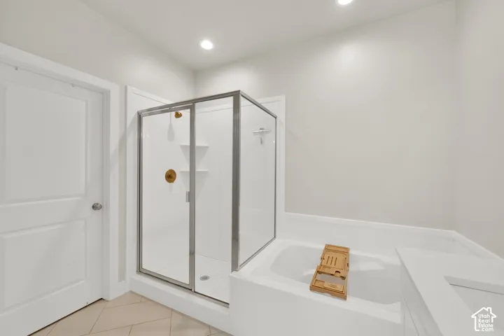Enclosed glass shower with integrated shelving, soaking tub, metallic shower fixtures, and tile flooring