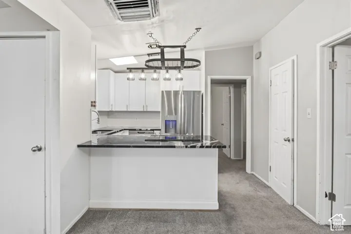 Kitchen featuring white cabinetry, dark stone-finish countertops, stainless steel refrigerator, and industrial-style hanging pendant lighting