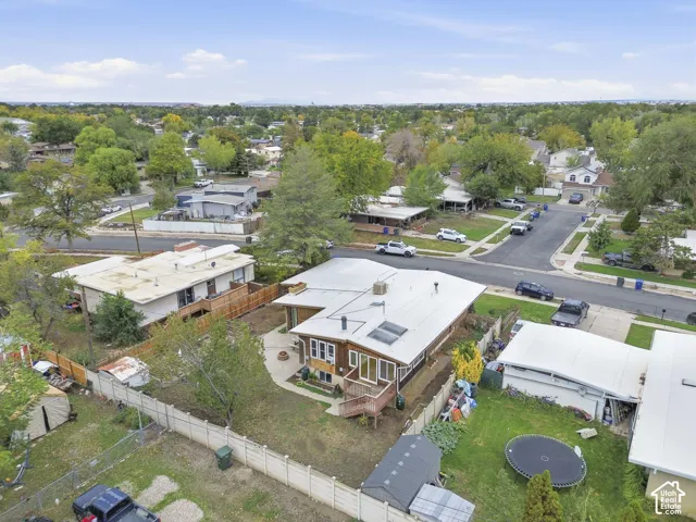Aerial perspective featuring a single-story residence with a metal roof, solar panels, attached wooden deck, and a fenced backyard