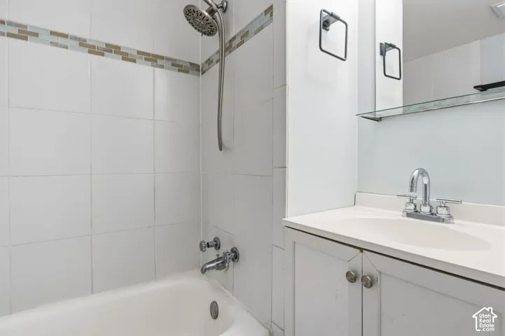 Bathroom featuring a white vanity with a composite countertop, polished chrome faucet, tiled shower surround with a mosaic accent border, and a wall-mounted medicine cabinet