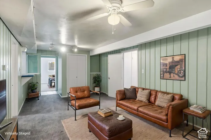 Vertical wood-paneled walls, neutral carpeting, ceiling fan with integrated lighting, and multiple interior doors with white finish
