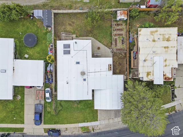 Aerial perspective of a property featuring a concrete rear patio, a fenced-in yard, designated garden beds, and a driveway with parking space