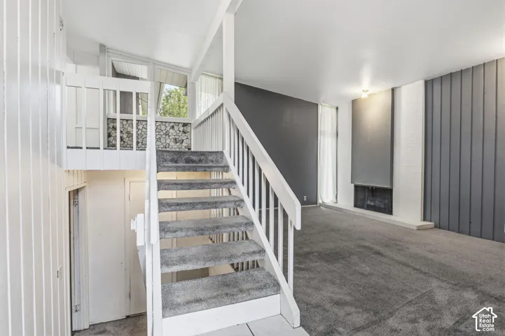 Living area featuring vaulted ceilings, floor-to-ceiling brick fireplace surround, vertical wood-paneled accent wall, and a railed staircase with a stone-accented landing