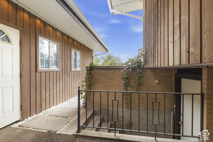 Vertical wood siding exterior featuring concrete paver walkway, brick retaining wall, and wrought iron railing