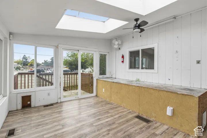 Sunroom featuring wood-finish flooring, a large overhead skylight, sliding glass doors, and a ceiling fan