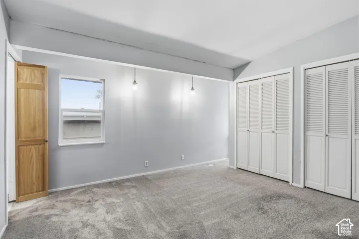 Room featuring dual sets of white louvered-door closets, neutral carpeting, recessed ceiling lighting, and a natural wood-finish door