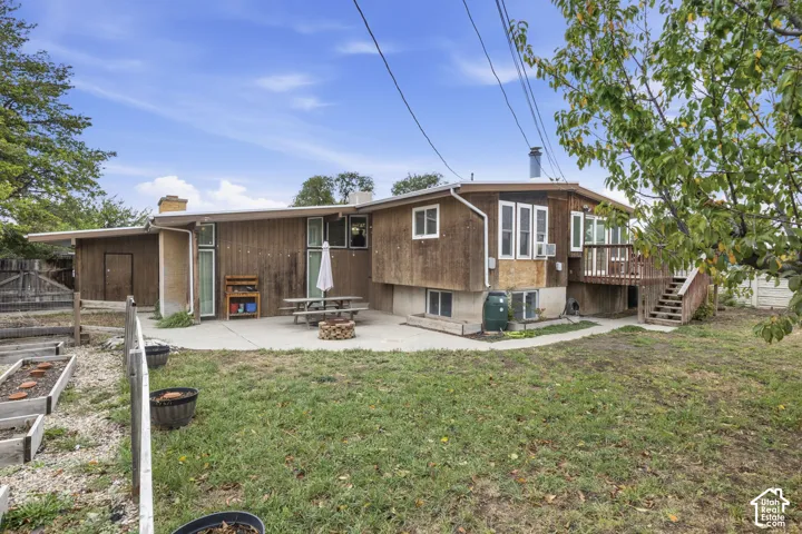 Exterior featuring wood siding, concrete patio, elevated wooden deck, and raised garden beds