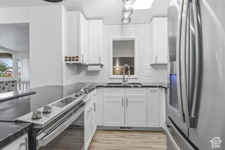 Kitchen featuring white shaker-style cabinetry, dark stone-finish countertops, subway tile backsplash, stainless steel appliances, and wood-finish flooring
