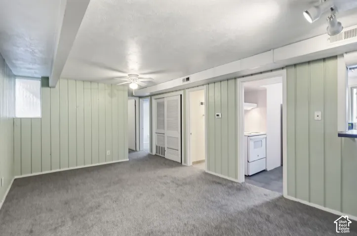 Room featuring vertical paneled walls, neutral carpeting, a ceiling-mounted light and fan fixture, and louvered bi-fold closet doors
