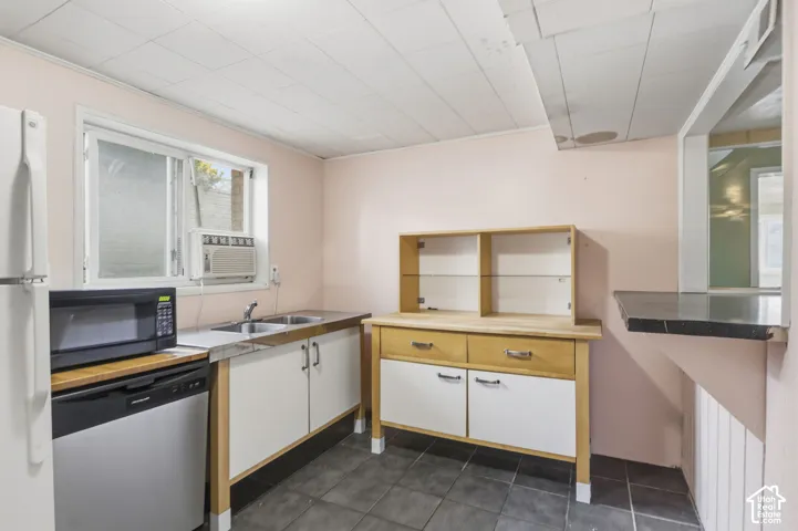 Kitchen area featuring tile flooring, dual-basin stainless steel sink, built-in wooden cabinetry with glass-front shelving, and a peninsula-style counter