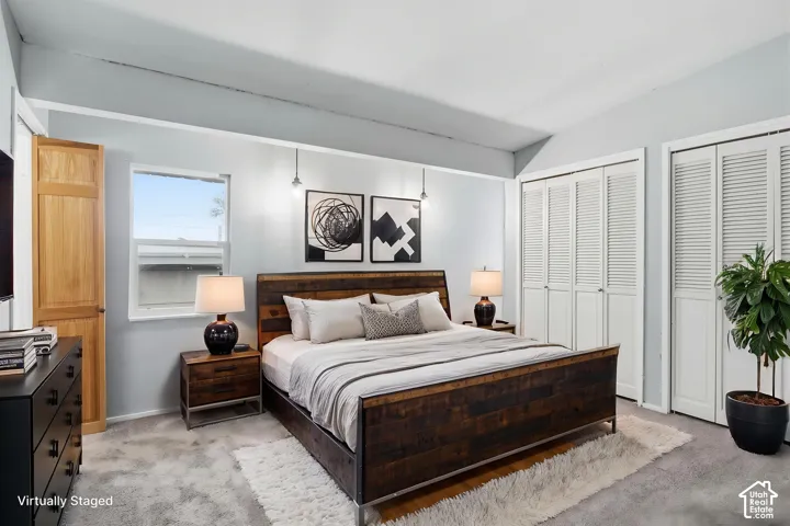Bedroom featuring vaulted ceilings, dual bi-fold closet doors, wall-mounted pendant lighting, and a single-hung window