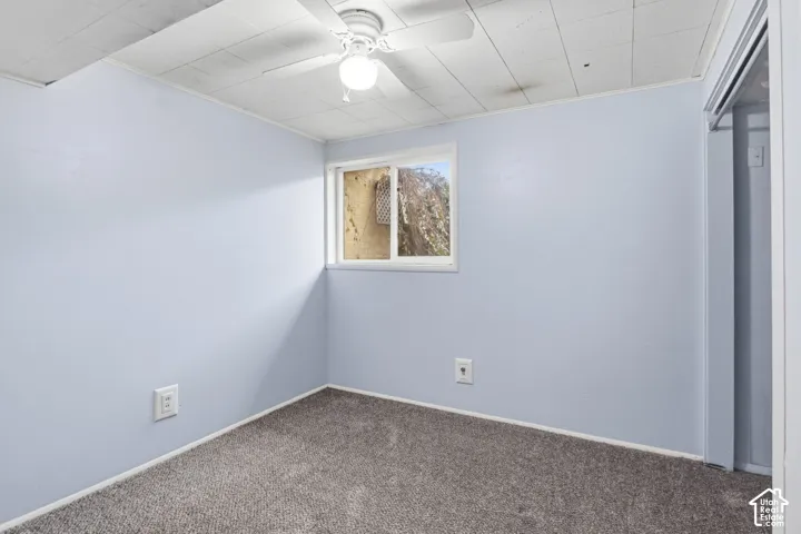 Room featuring gray carpeted flooring, a ceiling fan with integrated lighting, a sliding window, and a built-in closet