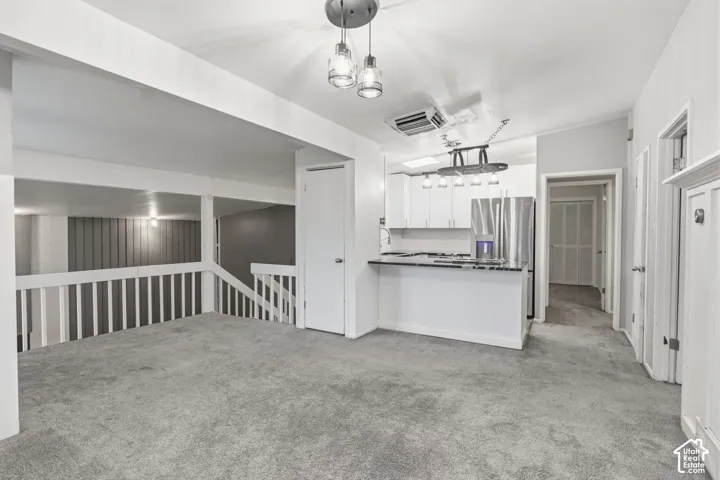 Open-concept interior featuring carpeted flooring, white cabinetry, a breakfast bar, metal pendant lighting, and a slatted balcony railing