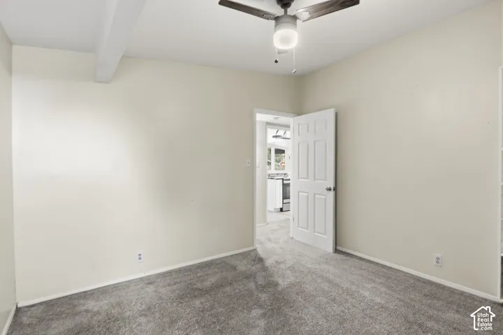 Interior room featuring neutral wall paint, wall-to-wall carpeting, a ceiling fan with integrated light fixture, and a six-panel interior door
