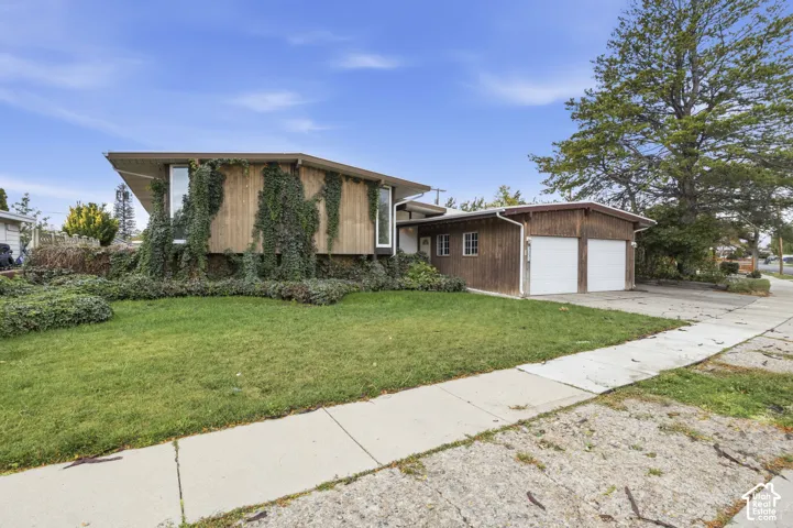 Mid-century architectural exterior featuring vertical wood siding, a low-pitch roofline, an attached two-car garage, and mature landscaping