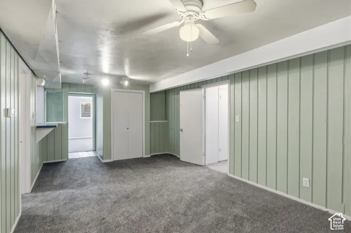 Interior space featuring vertical wood-panel wall treatments, neutral carpeting, a ceiling fan with integrated lighting, and multiple interior door enclosures