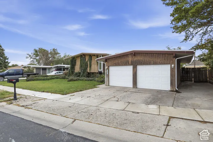 Mid-century architectural exterior featuring vertical wood siding, a double-car garage with white roll-up doors, and an attached carport