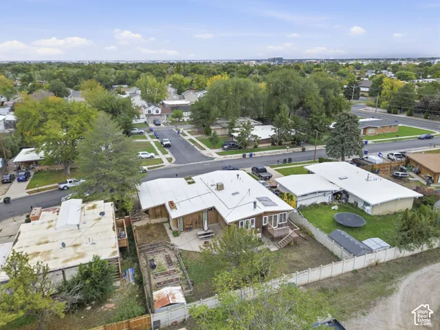 Aerial perspective of residential property featuring a concrete patio, multi-level roofline, fenced perimeter, and established trees