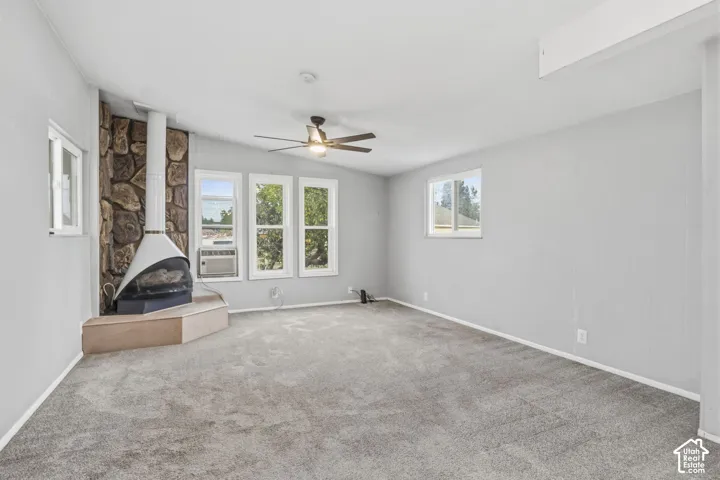Neutral-toned interior space featuring a stone-accented corner fireplace, mid-century style cone hearth, carpeted flooring, and a ceiling fan with integrated lighting