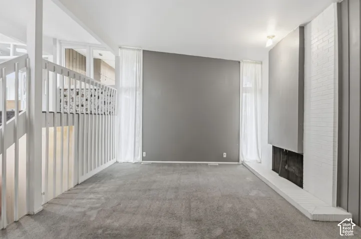 Vaulted ceilings, floor-to-ceiling windows, white-painted brick fireplace, and interior railing with vertical balusters