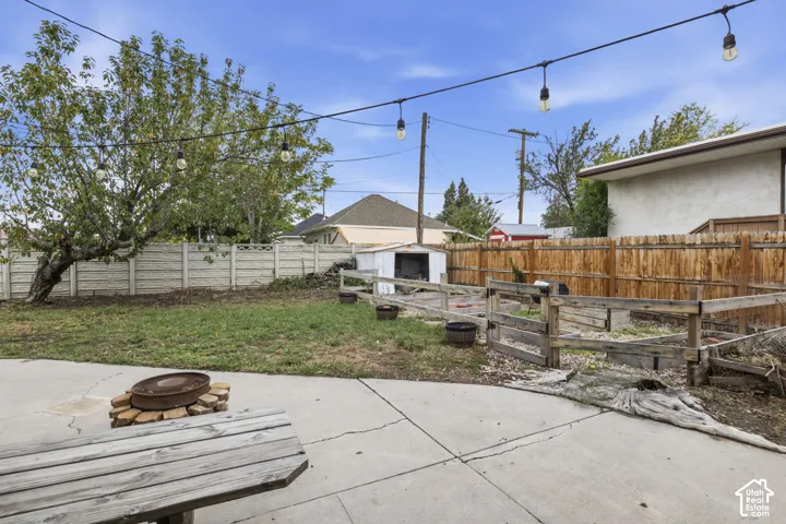 Backyard featuring a concrete patio, wood-finish perimeter fencing, raised planting beds, a storage structure, and overhead string lighting