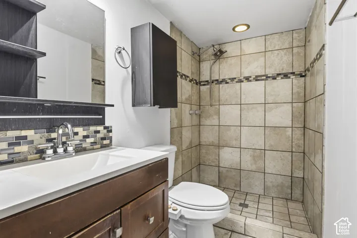 Bathroom featuring a wood-finish vanity with a white countertop, stone-tile shower surround with decorative mosaic inlay, recessed lighting, and a wall-mounted medicine cabinet