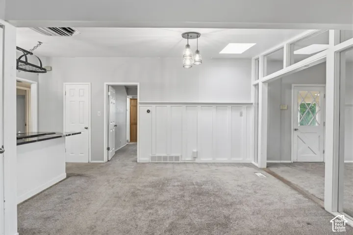Interior featuring white board-and-batten wainscoting, glass-paned exterior door, three-light pendant fixture, skylight, and wall-to-wall carpeting