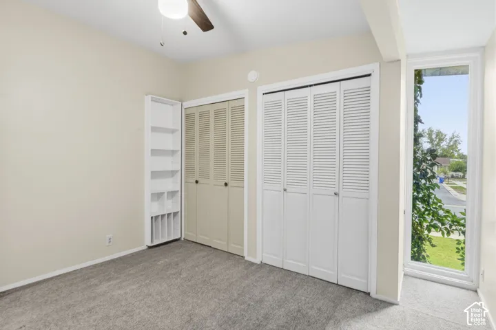 Full-height vertical window, dual louvered-door closets, built-in floor-to-ceiling shelving, and ceiling fan fixture