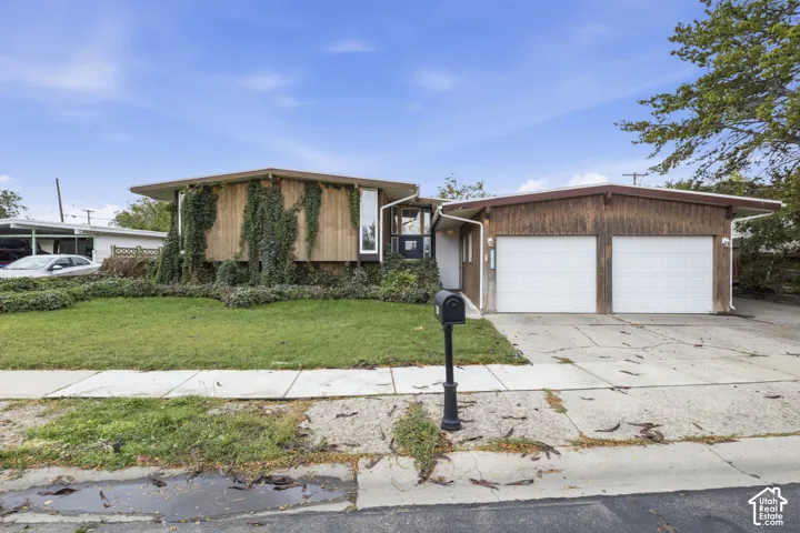Mid-century modern exterior featuring vertical wood siding, low-pitched rooflines, expansive dual-car garage, and established landscaping