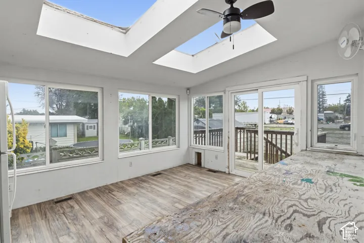 Sunroom featuring dual skylights, wood-finish flooring, sliding glass door access to an exterior deck, and multiple large windows