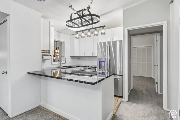 Kitchen featuring white cabinetry, dark stone-finish countertops, stainless steel refrigerator, white tile backsplash, and a metal hanging light fixture