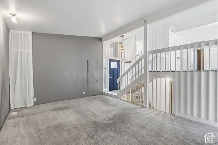 Vaulted ceiling, open staircase with white vertical balusters, textured wall detailing, and blue entry door with side light panels