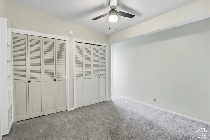 Room featuring neutral wall tones, wall-to-wall carpeting, dual bi-fold louvered closets, built-in shelving, and a ceiling fan with integrated lighting