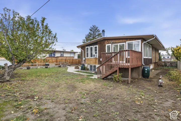 Exterior of the home featuring vertical wood siding, an elevated wood deck, a concrete patio, and a fenced yard with mature trees