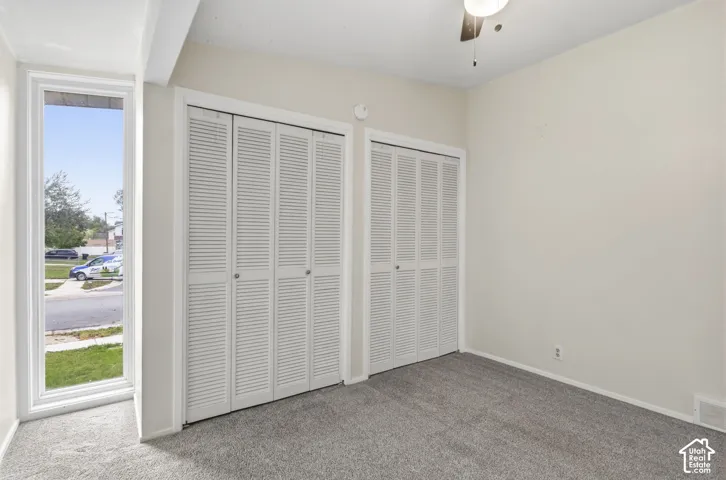 Room featuring dual floor-to-ceiling closets with white louvered doors, wall-to-wall carpeting, and a vertical window