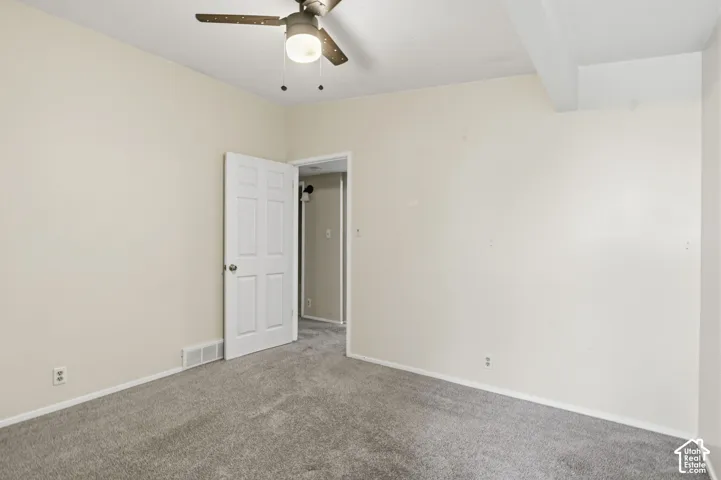 Room featuring neutral-toned carpeting, a central ceiling fan with integrated lighting, and a six-panel interior door