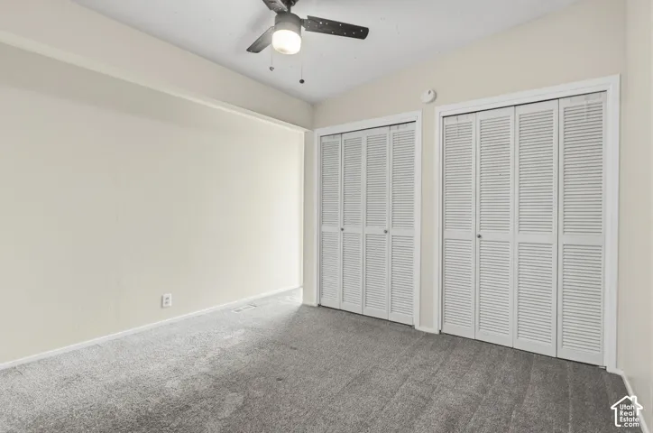 Room featuring neutral-toned carpeting, two sets of white louvered-door closets, and a ceiling-mounted fan with integrated light fixture