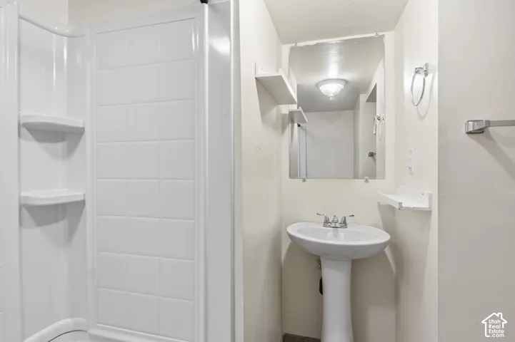 Shower stall with integrated shelving, white pedestal sink, polished chrome faucet, wall-mounted vanity mirror, and attached towel bar