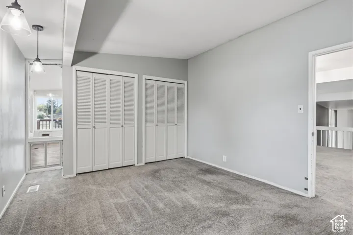 Room featuring neutral wall tones, wall-to-wall carpeting, dual bi-fold louvered closets, and dual pendant lighting fixtures