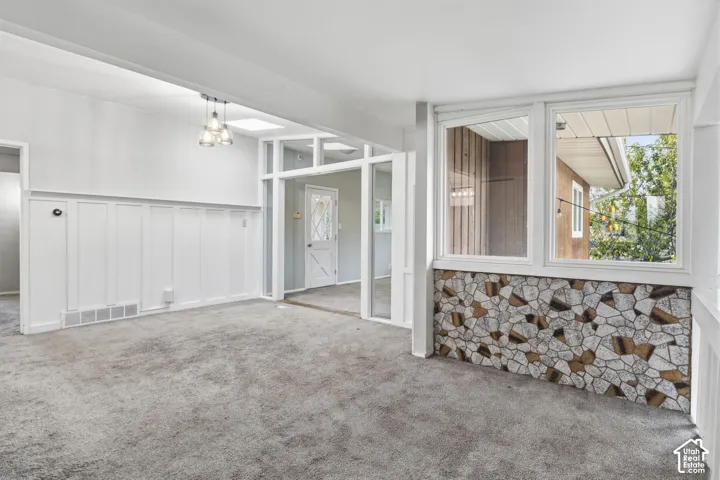 Interior space featuring white board-and-batten wainscoting, a decorative stone-clad knee wall under large windows, an integrated skylight, and a three-light glass pendant fixture