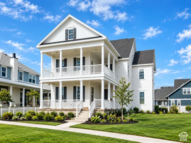 Two-story exterior featuring white horizontal siding, dual-level covered porches with column supports, dark-toned shutters, and professional landscaping