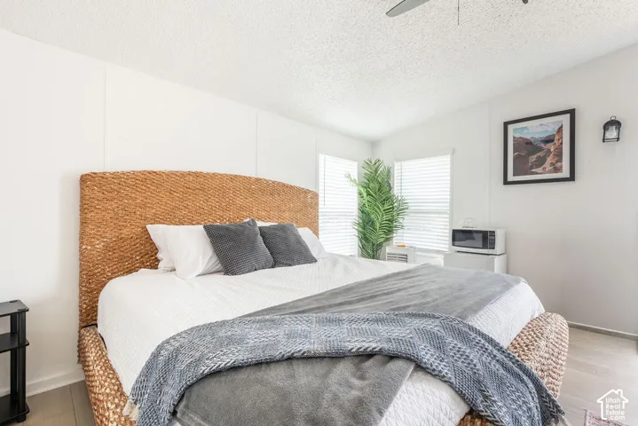 Bright interior space featuring wood-finish flooring, dual windows with horizontal blinds, a mounted wall sconce, and a ceiling fan