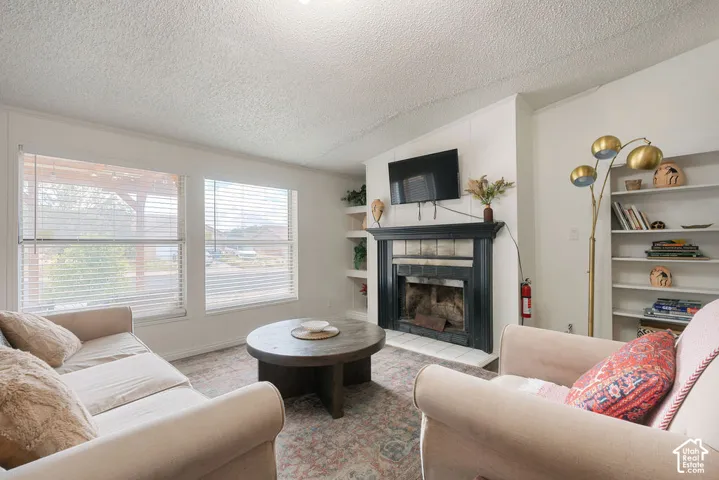 Living area featuring a fireplace with a black surround, built-in recessed shelving, textured ceiling, and dual windows