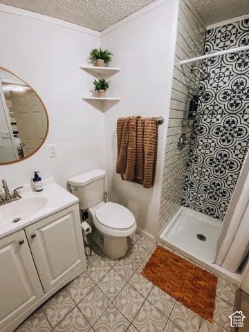 Bathroom featuring a white vanity cabinet with an integrated sink, patterned floor tile, shower with decorative accent tile and subway-style wall tile, round wall-mounted mirror, and floating corner shelving