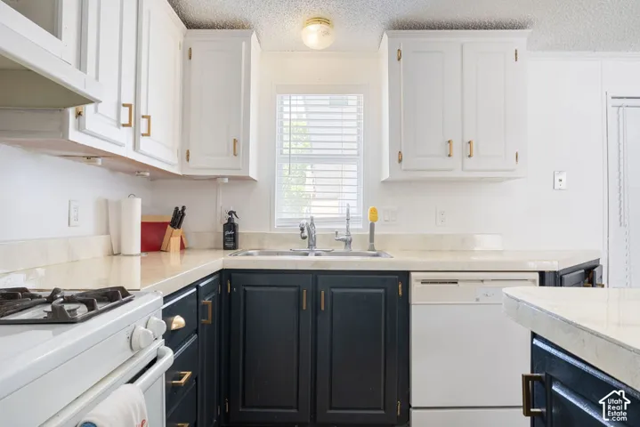 Kitchen featuring high-contrast two-tone cabinetry, solid surface countertops, dual-basin stainless steel sink, and metallic finish hardware
