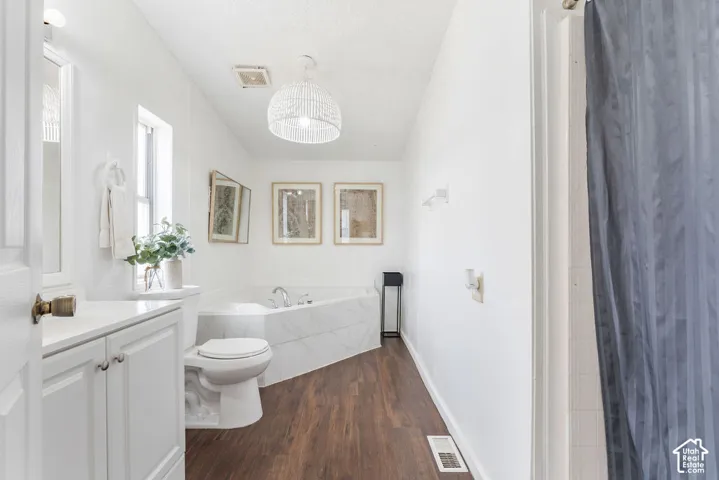 Bathroom featuring wood-finish flooring, a corner soaking tub with surround tile, white cabinetry, and a textured dome pendant light