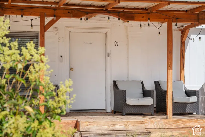 Covered front porch featuring wood support posts, a wood-plank deck, and exterior string lighting
