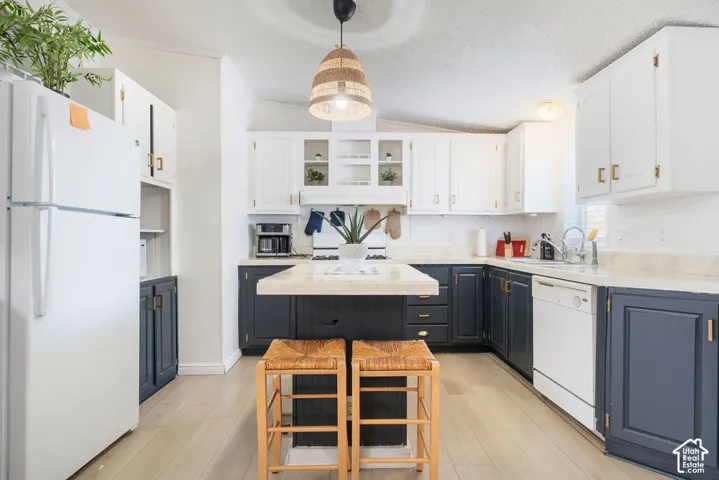 Kitchen featuring dual-tone cabinetry, central island with integrated seating, light-toned wood-finish flooring, and pendant lighting